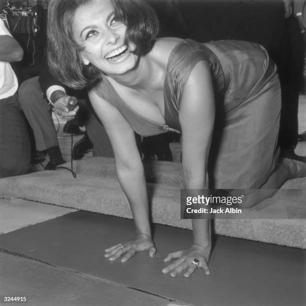 Italian actor Sophia Loren looks up and smiles while leaving imprints of her hands in wet cement at Grauman's Chinese Theater, Hollywood, California.