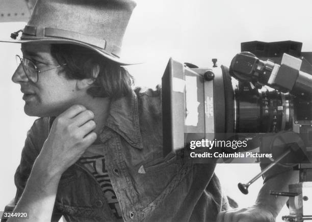 Profile view of American director Steven Spielberg working with a movie camera on the set of his film, 'Close Encounters of the Third Kind'.