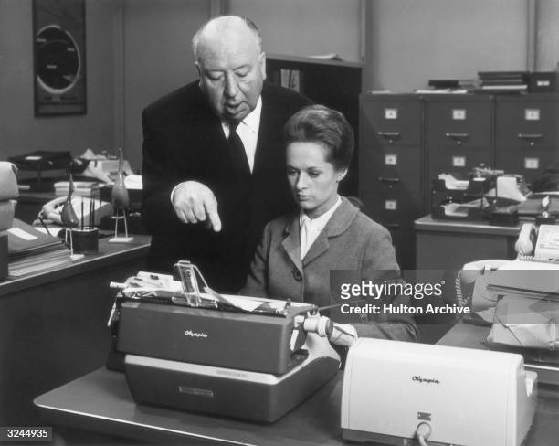British director Alfred Hitchcock directs American actor Tippi Hedren while she sits in front of a typewriter on the set of his film, 'Marnie'.