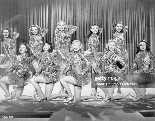 American actor Marilyn Monroe front row center), posing on one knee in a chorus line of women wearing sequined costumes with tutus in a still from...