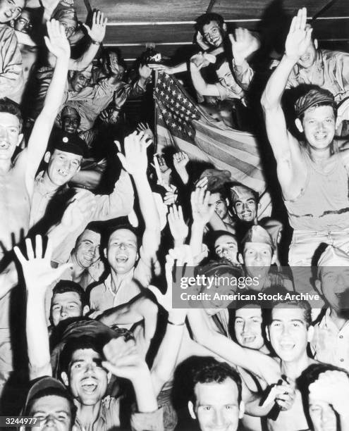 Allied prisoners of war wave their hands and an American flag as they cheer after being liberated at the Aomori Camp near Yokohama, Japan, World War...