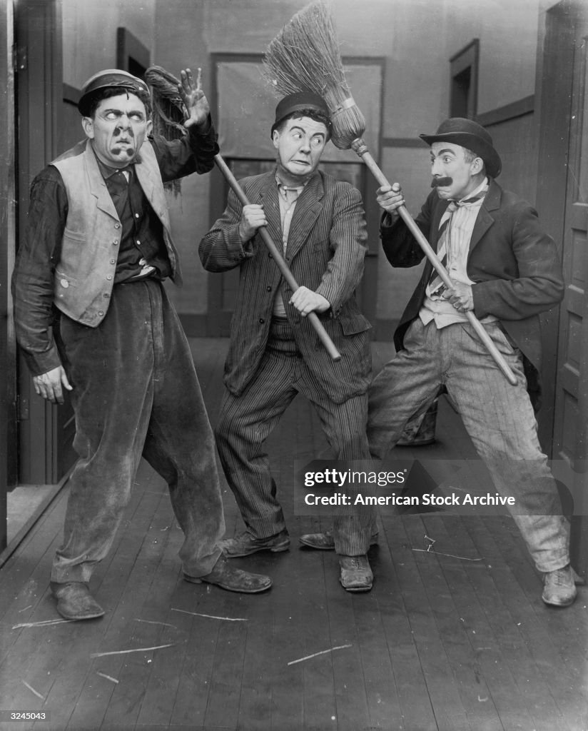 Three men clown with brooms in a still from a slapstick silent film ...