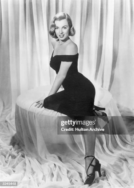 Full-length view of American actor Marilyn Monroe reclining in a black cocktail dress, in a promotional portrait for director John Huston's film 'The...