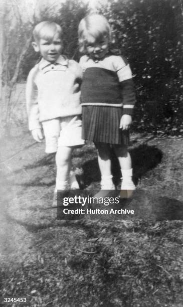 Childhood picture of American actor Marilyn Monroe at age four, standing with a little boy outdoors.