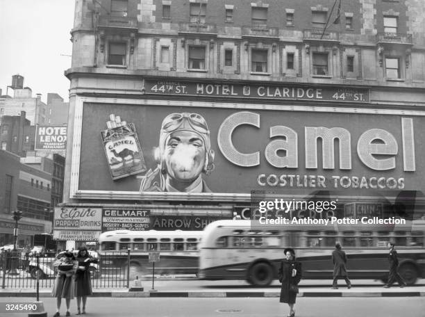 Street scene showing a Camel cigarette billboard with a pilot's face smoking on the exterior of the Claridge Hotel in Times Square, New York City.