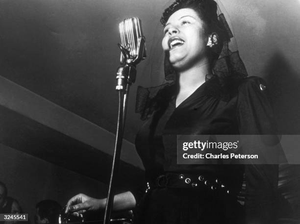 American jazz singer Billie Holiday sings in front of a microphone at a Sunday afternoon jam session at Ryan's on 52nd Street, New York City.