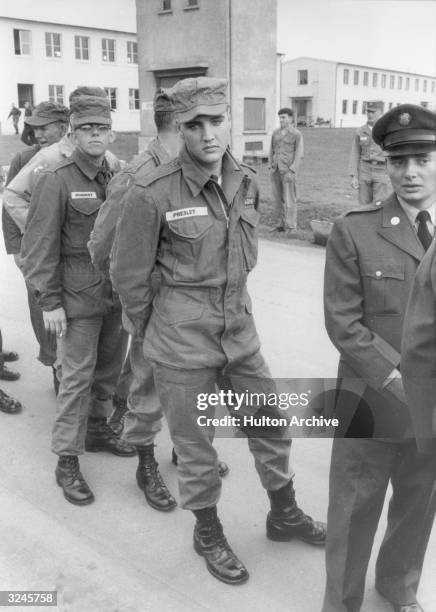 American rock n' roll singer and United States Army private Elvis Presley stands in line with other enlisted men and officers on a military base,...