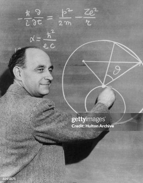 Italian-born physicist Dr. Enrico Fermi draws a diagram at a blackboard with mathematical equations.