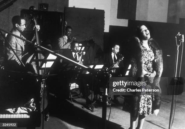 American jazz singer Billie Holiday performs with, left to right; bassist Johnny Williams, trumpeter Frankie Newton and saxophonists Stan Payne and...