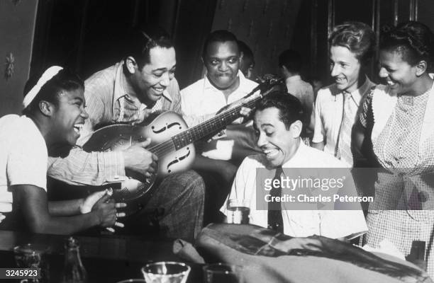 American composer and bandleader Duke Ellington plays guitar and Cab Calloway plays piano during a jam session at a private party hosted by Hearst...