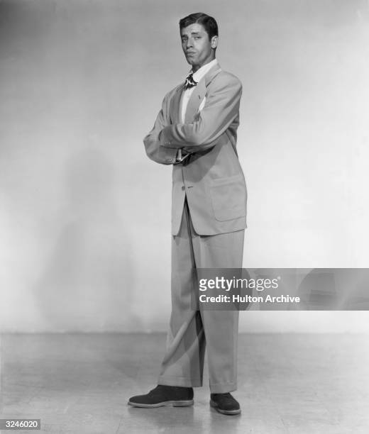 Full-length promotional studio portrait of American actor and comedian Jerry Lewis standing with his arms folded on his chest.