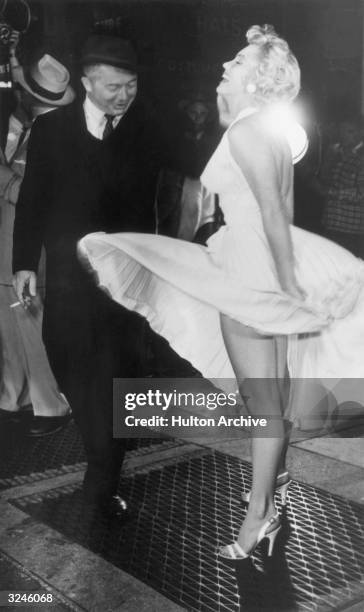 American actor Marilyn Monroe stands on a subway grate and laughs as the wind blows the skirt of her white halter dress next to Austrian-born...