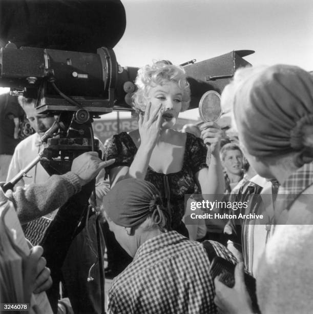 American actor Marilyn Monroe adjusts her make-up, using a handheld mirror on the set of director Joshua Logan's film, 'Bus Stop'. She is standing...