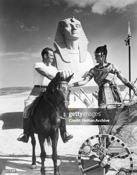 American actor Charlton Heston rides on horseback while shaking hands with Russian-born actor Yul Brynner , who stands in a chariot prior to the...