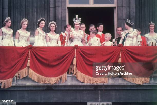 The newly crowned Queen Elizabeth II waves to the crowd from the balcony at Buckingham Palace. Her children Prince Charles and Princess Anne stand...