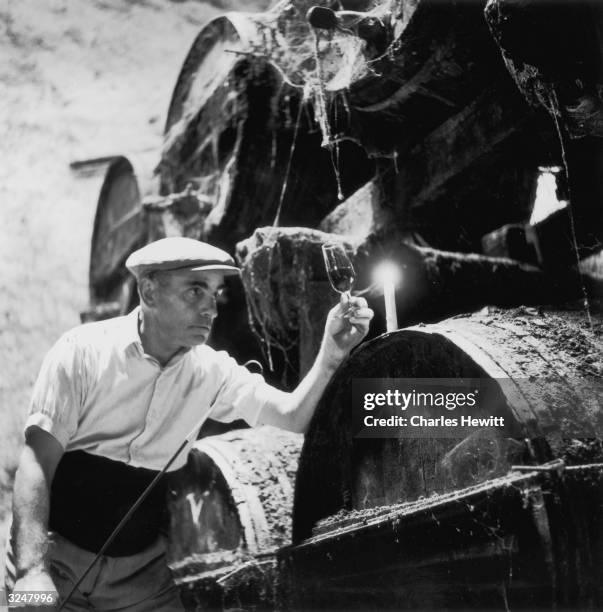 Man examining the colour of a glass of sherry by the light of a candle in a wine cellar at Jerez in Spain. Original Publication: Picture Post - 6734...