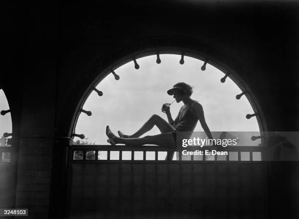 Young woman is silhouetted in an archway as she enjoys a cooling drink at Finchley Baths in north London.