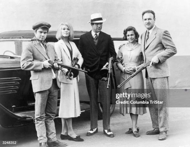 Cast members from director Arthur Penn's film, 'Bonnie & Clyde,' pose with machine guns in front of a car. Left to right: Michael J Pollard, Faye...