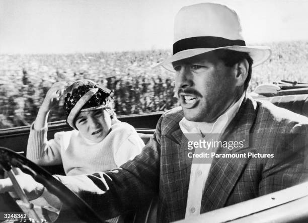 American actor Ryan O'Neal drives a car while his daughter, American actor Tatum O'Neal, holds on to her hat in the passenger's seat in a still from...