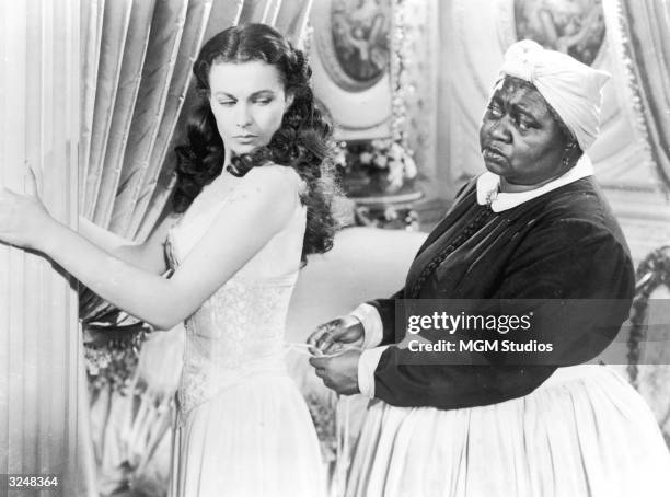 British actor Vivien Leigh holds on to a pillar as American actor Hattie McDaniel tightens her corset in a still from the film, 'Gone with the Wind,'...