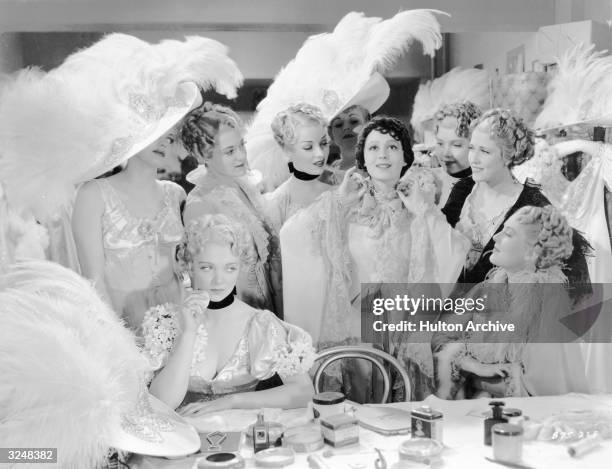 American actor Virginia Bruce sits nearby pouting as German-born actor Luise Rainer gets the attention of their fellow performers in a dressing room...