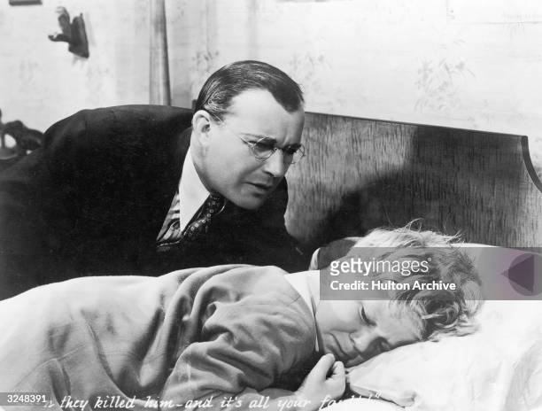 American actor Willard Robertson comforts American child actor Jackie Cooper, who lies in bed in a still from the film, 'Skippy,' directed by Norman...