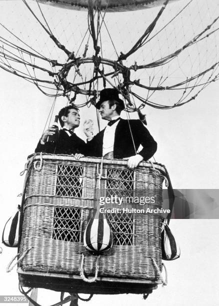 Mexican actor Cantinflas and British actor David Niven toast with champagne while riding in a hot air balloon basket in a still from the film,...