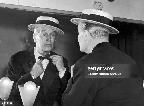 French singer and actor Maurice Chevalier ties his bow tie as he prepares for his one man show at the Palace Theatre, London, England.