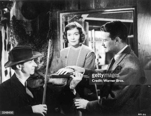 American actor Lew Ayres holds the hand of American actor Jane Wyman and places it upon a musician's fiddle in a still from director Jean Negulesco's...