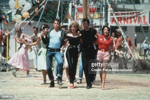 Actors Jeff Conaway, Olivia Newton-John, John Travolta and Stockard Channing walk arm in arm at a carnival in a still from the film, 'Grease'...