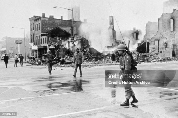 Black man crosses a street past soldiers and a bombed building during the race riots that followed Martin Luther King's assassination, Washington, DC.