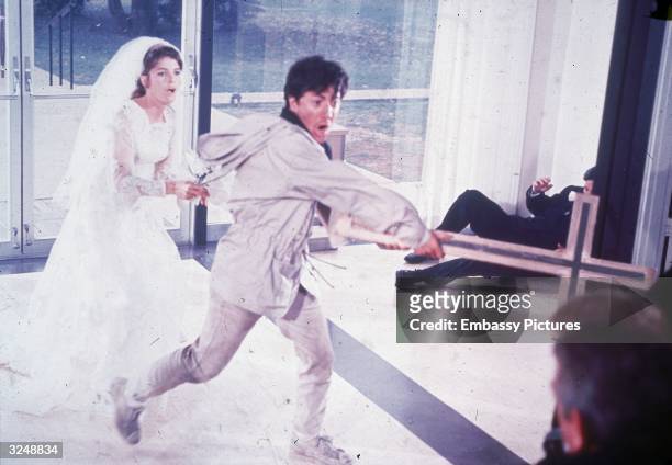 American actor Dustin Hoffman uses a cross as a weapon to keep people away while he attempts to flee a church with American actor Katharine Ross, in...