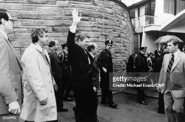 Surrounded by police officers and FBI agents, American statesman Ronald Reagan, the 40th President of the United States of America, waves to...