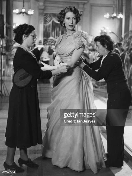British actress Valerie Hobson being dressed in a Sophie Harris creation by her personal dresser and a studio wardrobe assistant, for a ballroom...