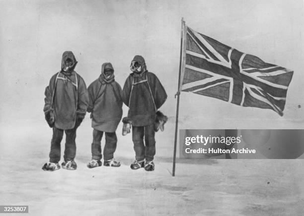 Irish explorer Sir Ernest Henry Shackleton and two members of his expedition team beside a Union Jack within 111 miles of the South Pole, a record...