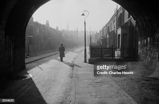 Solitary figure walks down a deserted street in London's East End, which London County Council plans to redevelop as part of its post-war rebuilding...