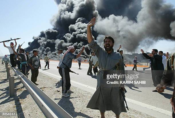 Iraqi Sunni Muslim insurgents celebrate in front of a burning US convoy they have attacked earlier 08 April 2004 in Abu Gharib, on the outskirts of...
