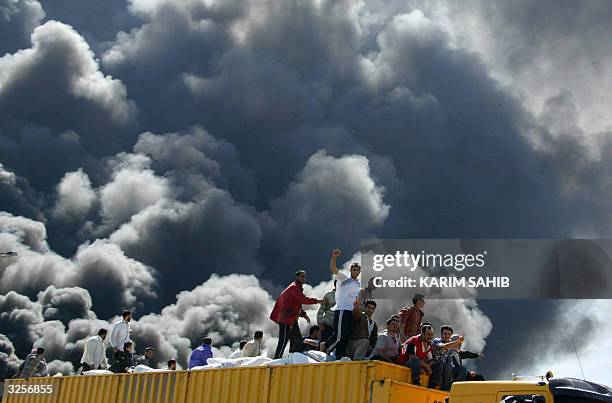 Iraqis sitting on a truck loaded with medical and food supplies bound for the flashpoint town of Fallujah, pass a burning US convoy attacked 08 April...