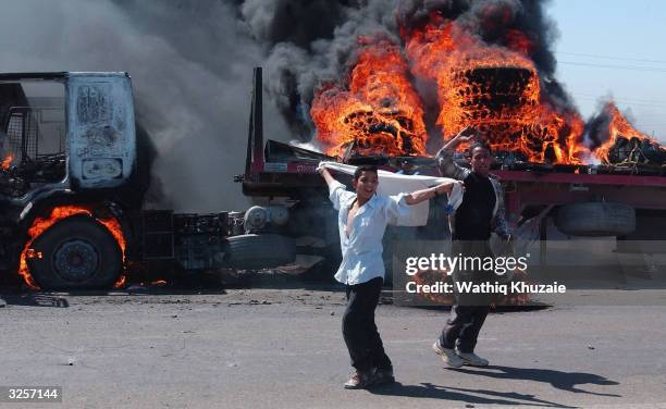 Crowd of Iraqis loyal to radical Shia cleric Moqtada al-Sadr cheer after attacking and burning two vehicles in a convoy of auto parts and fuel trucks...