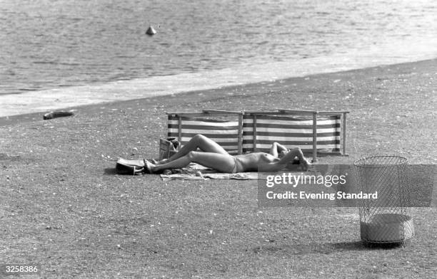 Am in Hyde Park by the banks of the Serpentine, a young woman takes advantage of the sun's rays and sunbathes topless.