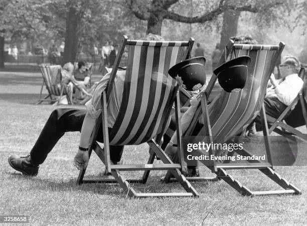 Two London policemen take the weight off their feet during the May heatwave, whilst patrolling in the park.