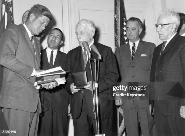American poet Robert Frost is presented with a medal by President John F Kennedy at the White House, in turn the president received a book of poems...