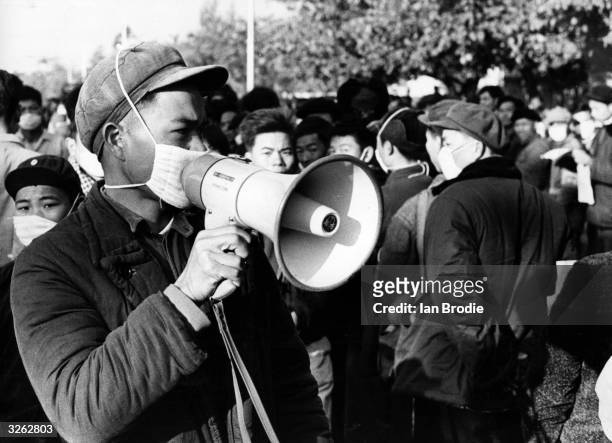Members of the Red Guards in China, their mouths masked against flu germs on the orders of Chairman Mao, address the passing crowds as part of the...
