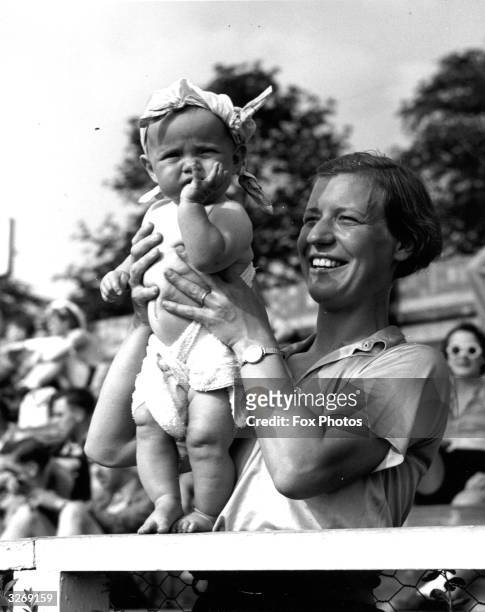 Baby wearing a handkerchief on its head to protect it from the sun is held up by its mother during an international bicycle polo match between...