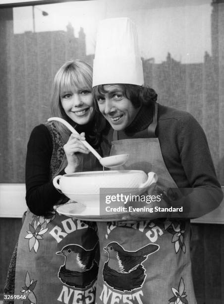 Tessa Wyatt and Richard O'Sullivan, on the set of the British TV comedy series 'Robin's Nest', wearing pinafores bearing the show's name, and holding...