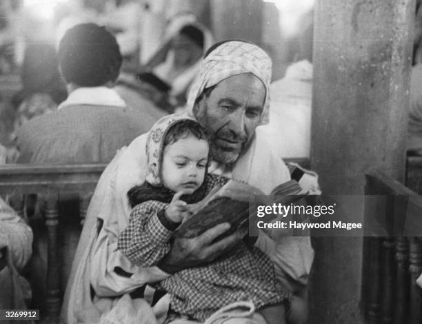 An elderly Jewish man studies a prayer book with a small child in a synagogue on the island of Djerba or Jarbah, off eastern Tunisia. They are there...