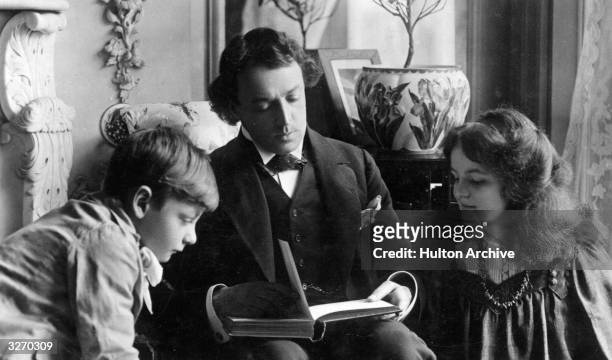 Portrait of actor John Martin Harvey reading to two children on a postcard.