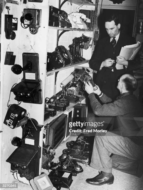 Property master Bert Guitens and an assistant check over the collection of telephones held in the property room at Pinewood Studios, Iver Heath,...