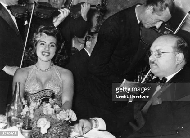Violinists serenading ex-King Farouk of Egypt with his latest female companion Miss Naples, 18-year-old Irma Minutolo, at a Monte Carlo casino.
