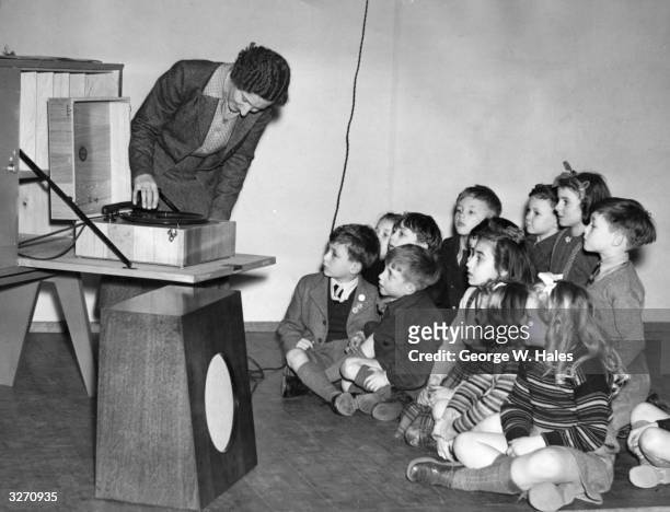 Teacher at Lewisham junior school, London, which has been rebuilt after being destroyed in the Blitz, uses modern methods such as the radiogram to...